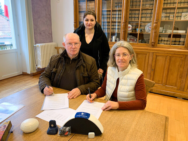 Signature de convention entre CCAS et présence verte Photo deux personnes à table, une derrière eux, signature de la convention présence verte